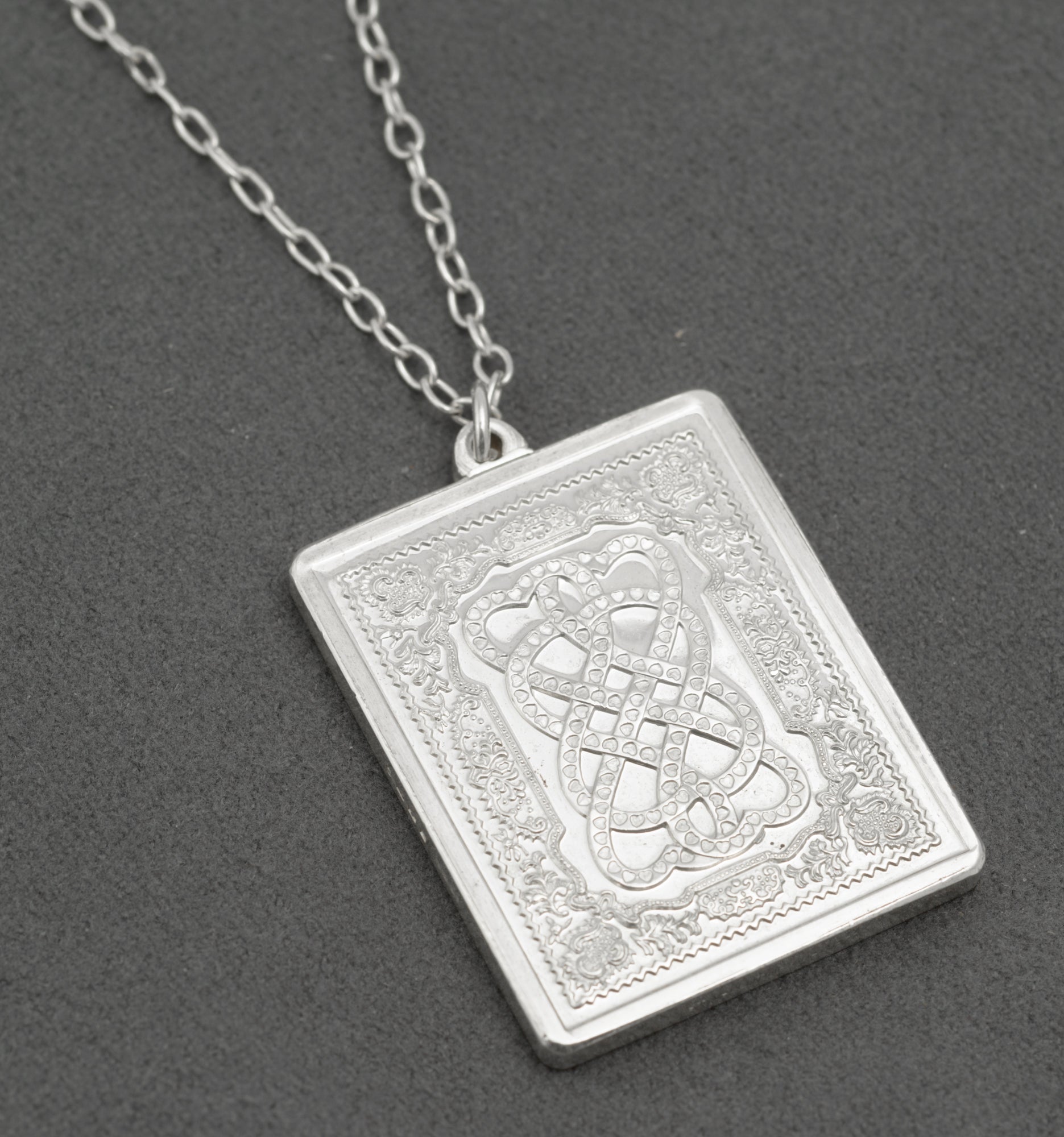 Vintage sterling silver St Valentine's Day ingot pendant by John Pinches 1977 showing Celtic interlaced knotwork with heart shapes on stippled ground within acanthus scrolling border on grey background with silver chain