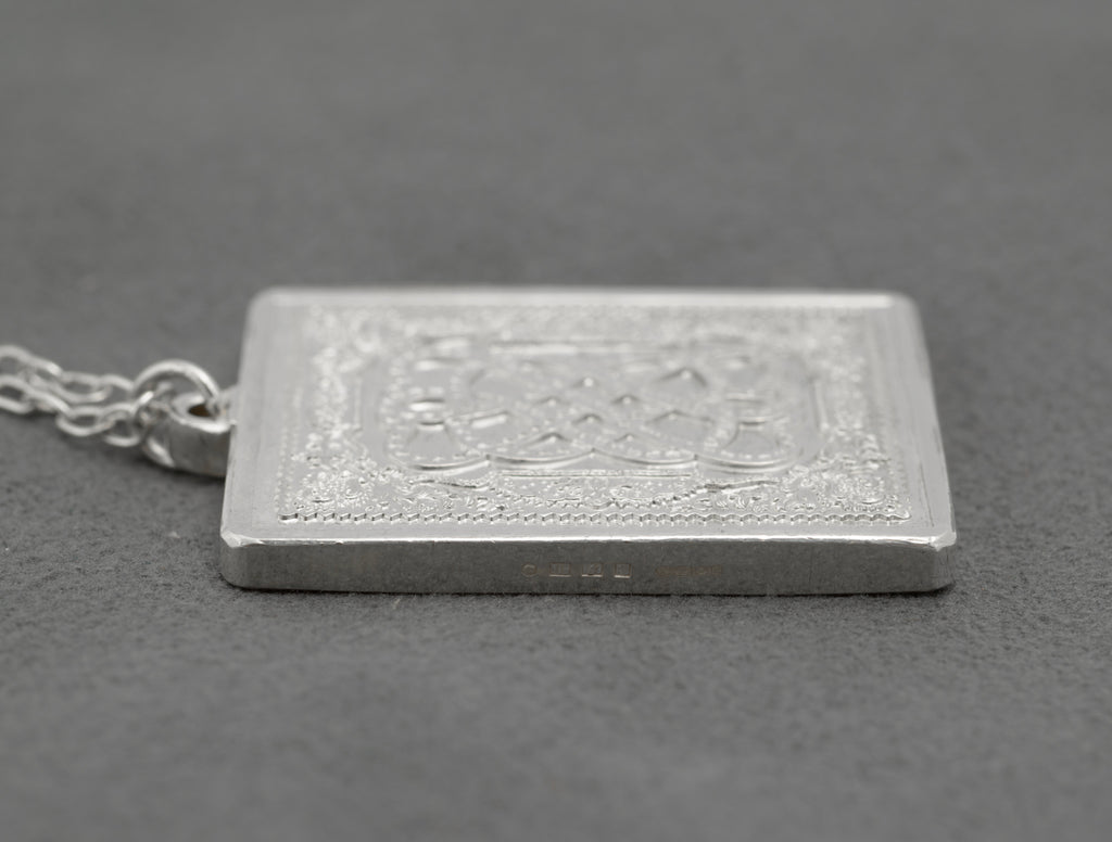 Side profile of vintage sterling silver John Pinches St Valentine's Day 1977 ingot pendant showing genuine ingot depth with SILVER 925/1000 mark visible on edge on grey background
