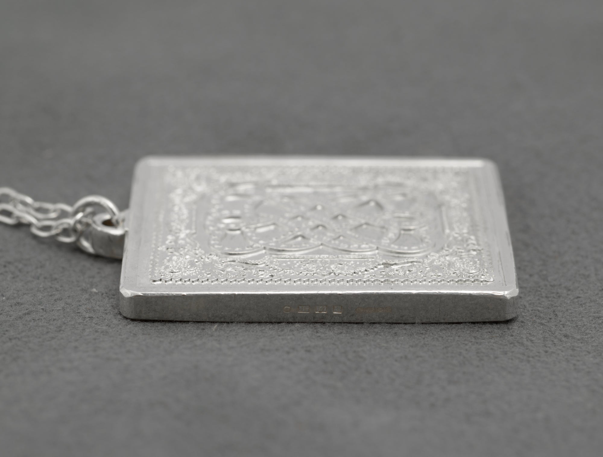 Side profile of vintage sterling silver John Pinches St Valentine's Day 1977 ingot pendant showing genuine ingot depth with SILVER 925/1000 mark visible on edge on grey background