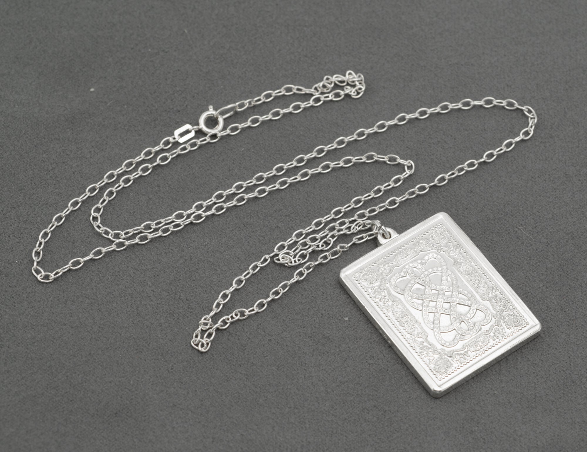 Full length view of vintage sterling silver John Pinches 1977 St Valentine's Day Celtic knotwork pendant on 61cm silver cable chain with spring ring clasp on grey background