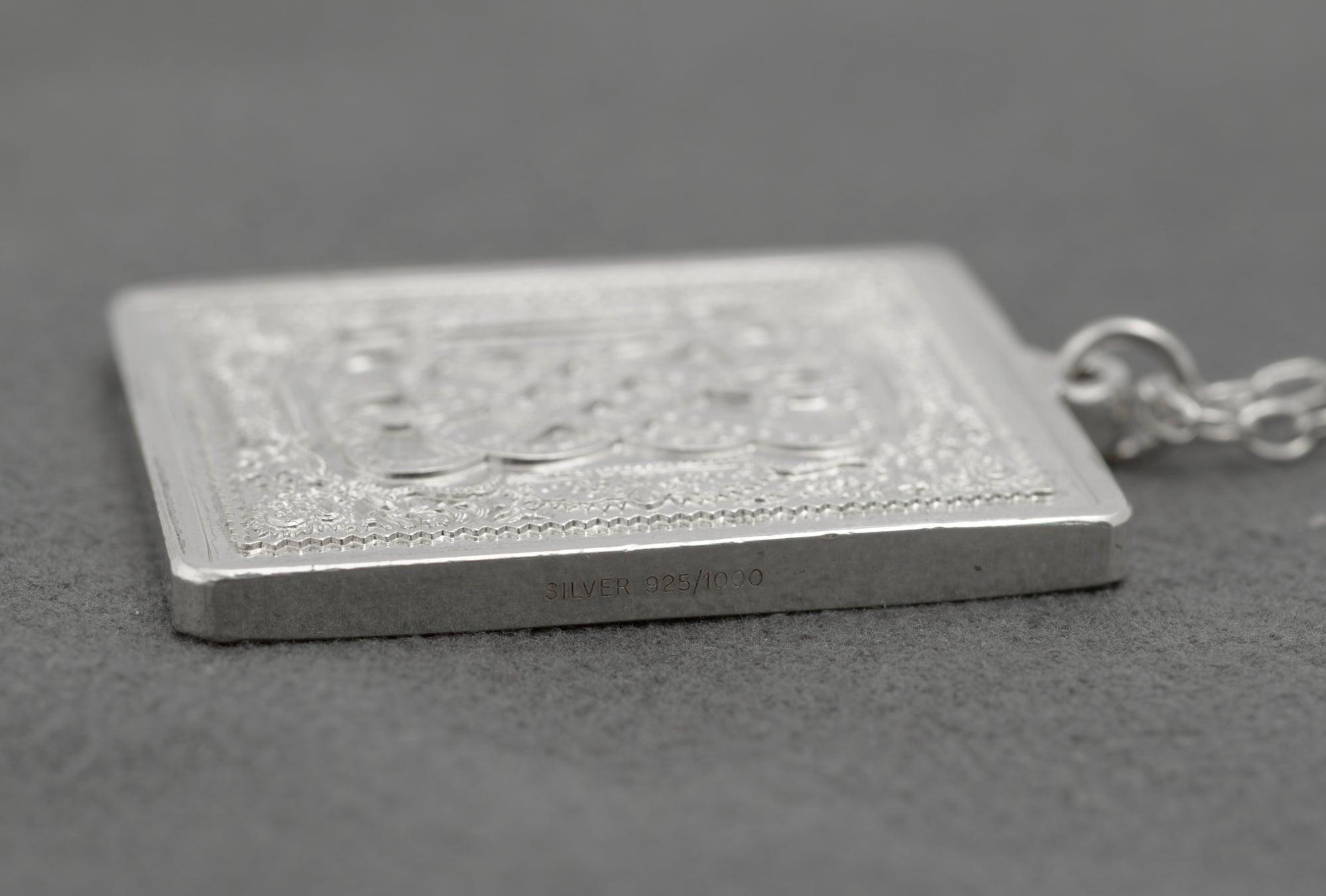 Close up side edge of vintage sterling silver John Pinches 1977 St Valentine's Day ingot pendant showing SILVER 925/1000 hallmark stamp on pendant edge on grey background