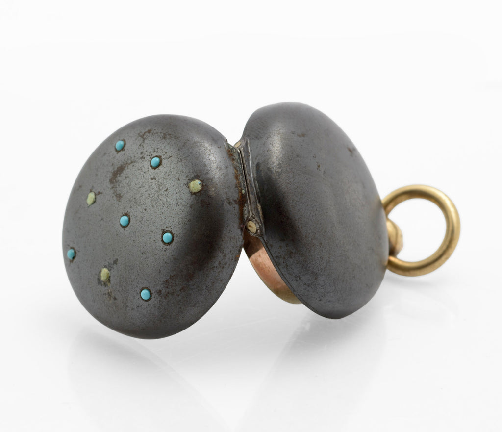 Antique gun metal sovereign case with turquoise cabochons laid flat next to 20p coin showing scale approximately 33mm diameter on white background