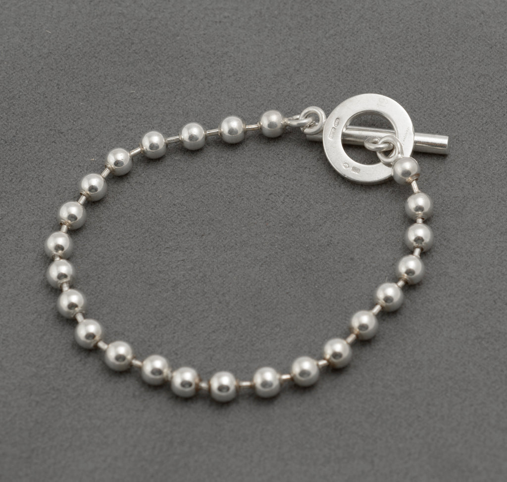 Gucci sterling silver boule ball link bracelet with T-bar toggle clasp laid in circle on dark grey background showing polished 5mm ball links and toggle ring front face