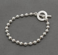Gucci sterling silver boule ball link bracelet with T-bar toggle clasp laid in circle on dark grey background showing polished 5mm ball links and toggle ring front face