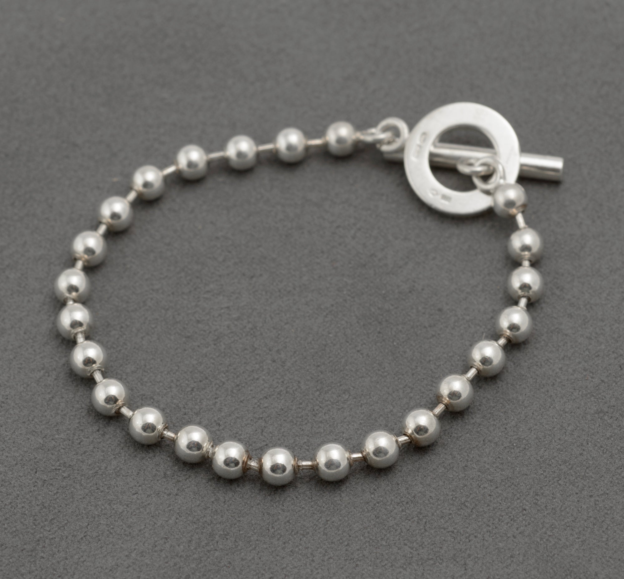 Gucci sterling silver boule bracelet close up of T-bar toggle clasp showing plain polished front face of circular ring with ball link chain on dark grey background