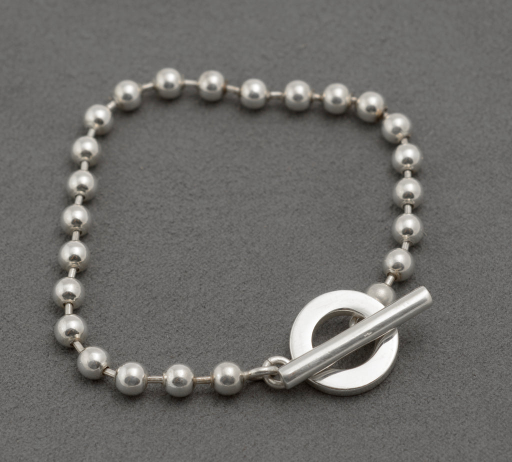 Gucci sterling silver boule bracelet showing T-bar toggle clasp from front with cylindrical T-bar and circular ring against polished ball link chain on dark grey background