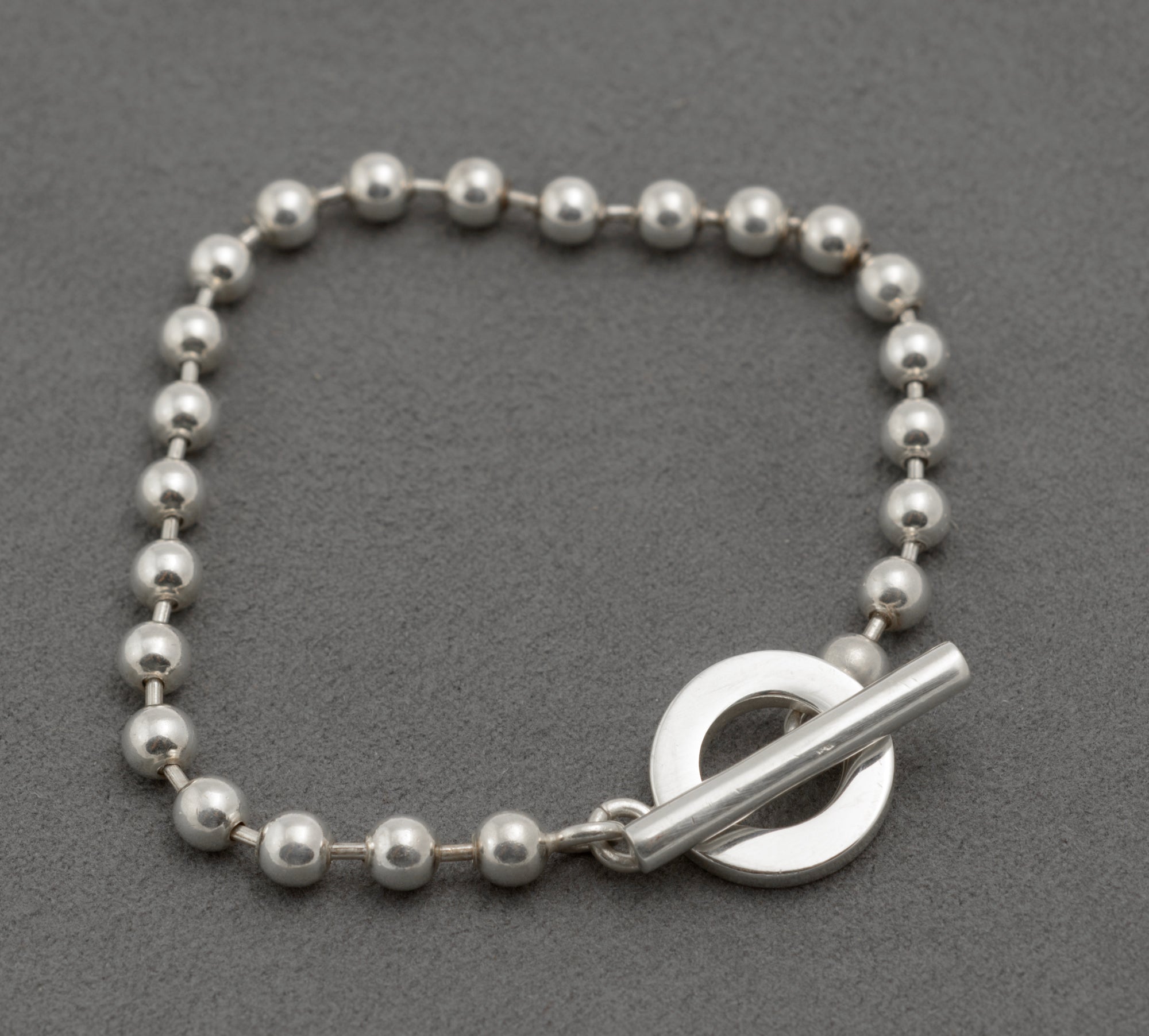 Gucci sterling silver boule bracelet showing T-bar toggle clasp from front with cylindrical T-bar and circular ring against polished ball link chain on dark grey background