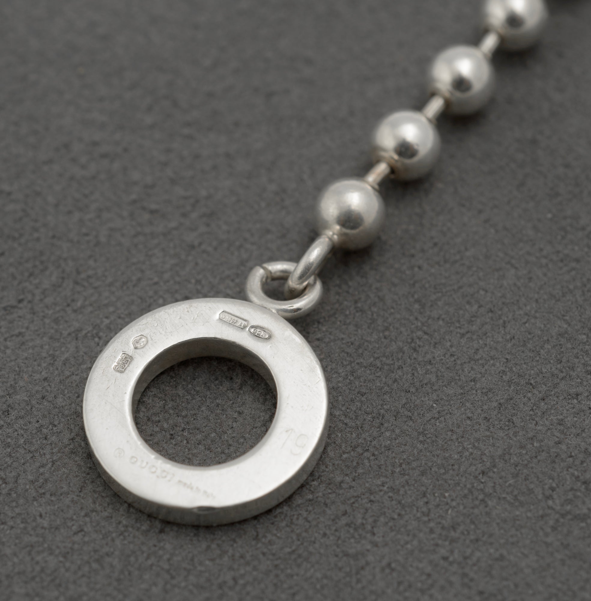 Reverse of Gucci sterling silver bracelet toggle ring showing Gucci Made in Italy copyright mark Italian hallmark 925 silver mark International Convention mark and maker registration 1697 AR on dark grey background