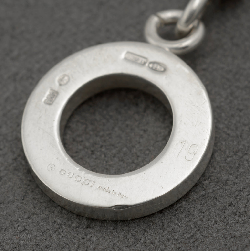Close up reverse of Gucci sterling silver bracelet toggle ring showing full hallmark suite including copyright Gucci Made in Italy 925 International Convention mark and 1697 AR Freschi Vangelisti maker registration on dark grey background