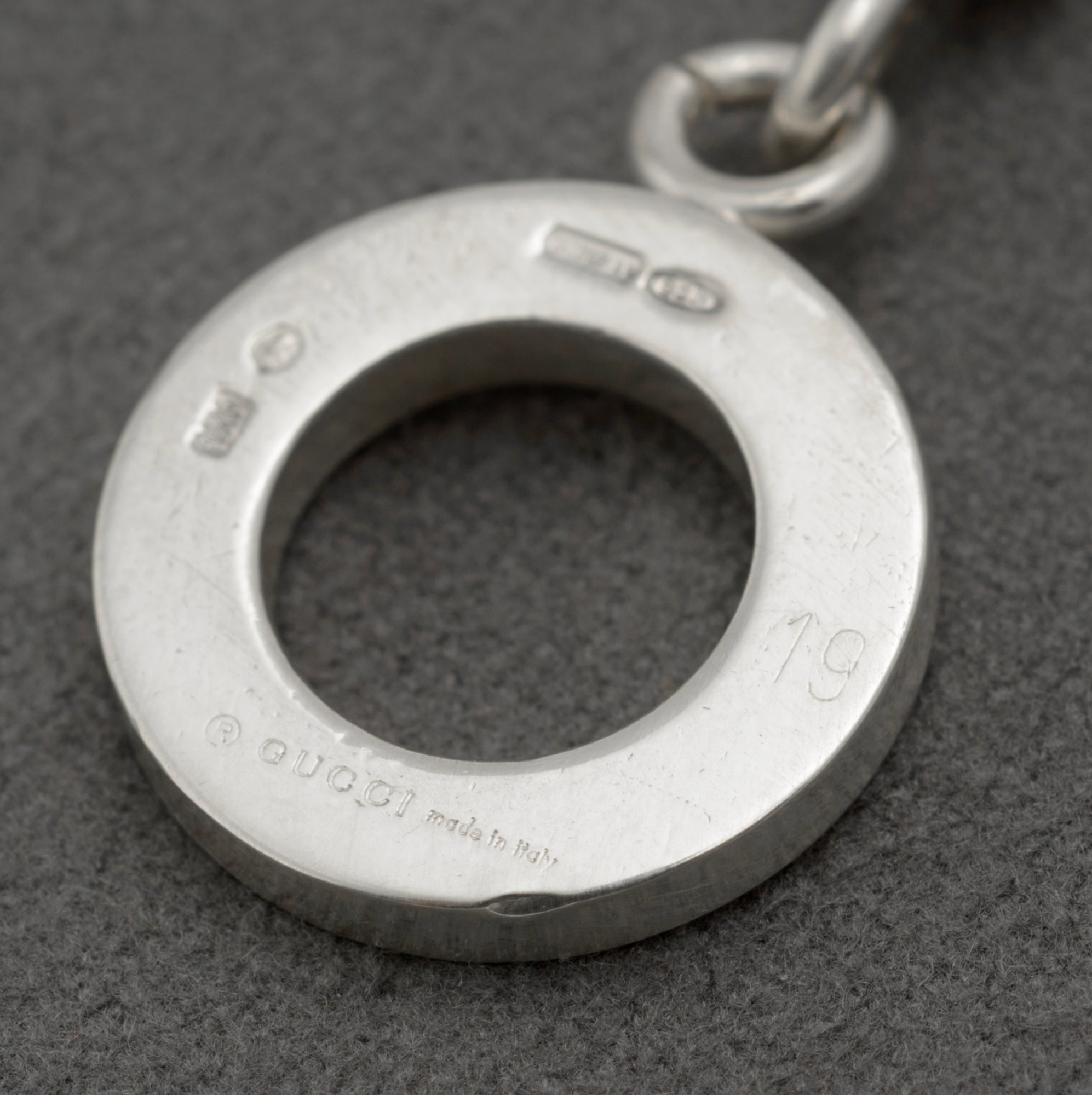 Close up reverse of Gucci sterling silver bracelet toggle ring showing full hallmark suite including copyright Gucci Made in Italy 925 International Convention mark and 1697 AR Freschi Vangelisti maker registration on dark grey background
