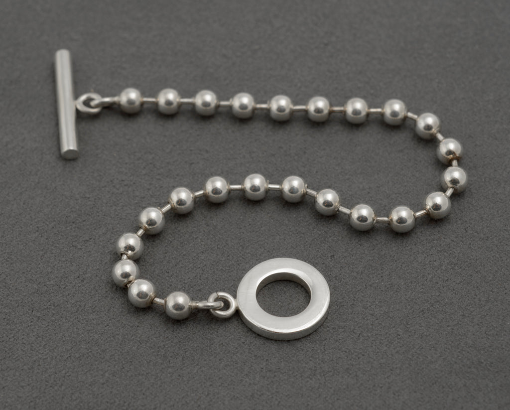 Gucci sterling silver boule ball link bracelet laid straight on dark grey background showing full 20cm length T-bar toggle clasp and evenly spaced 5mm polished ball links