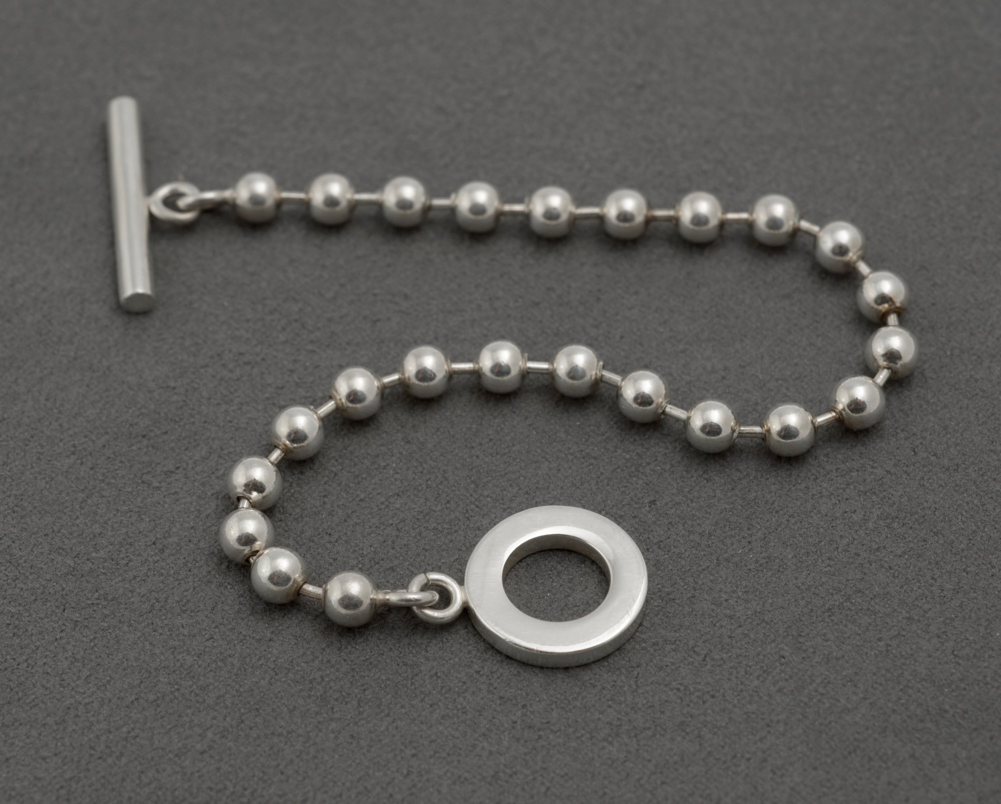 Gucci sterling silver boule ball link bracelet laid straight on dark grey background showing full 20cm length T-bar toggle clasp and evenly spaced 5mm polished ball links