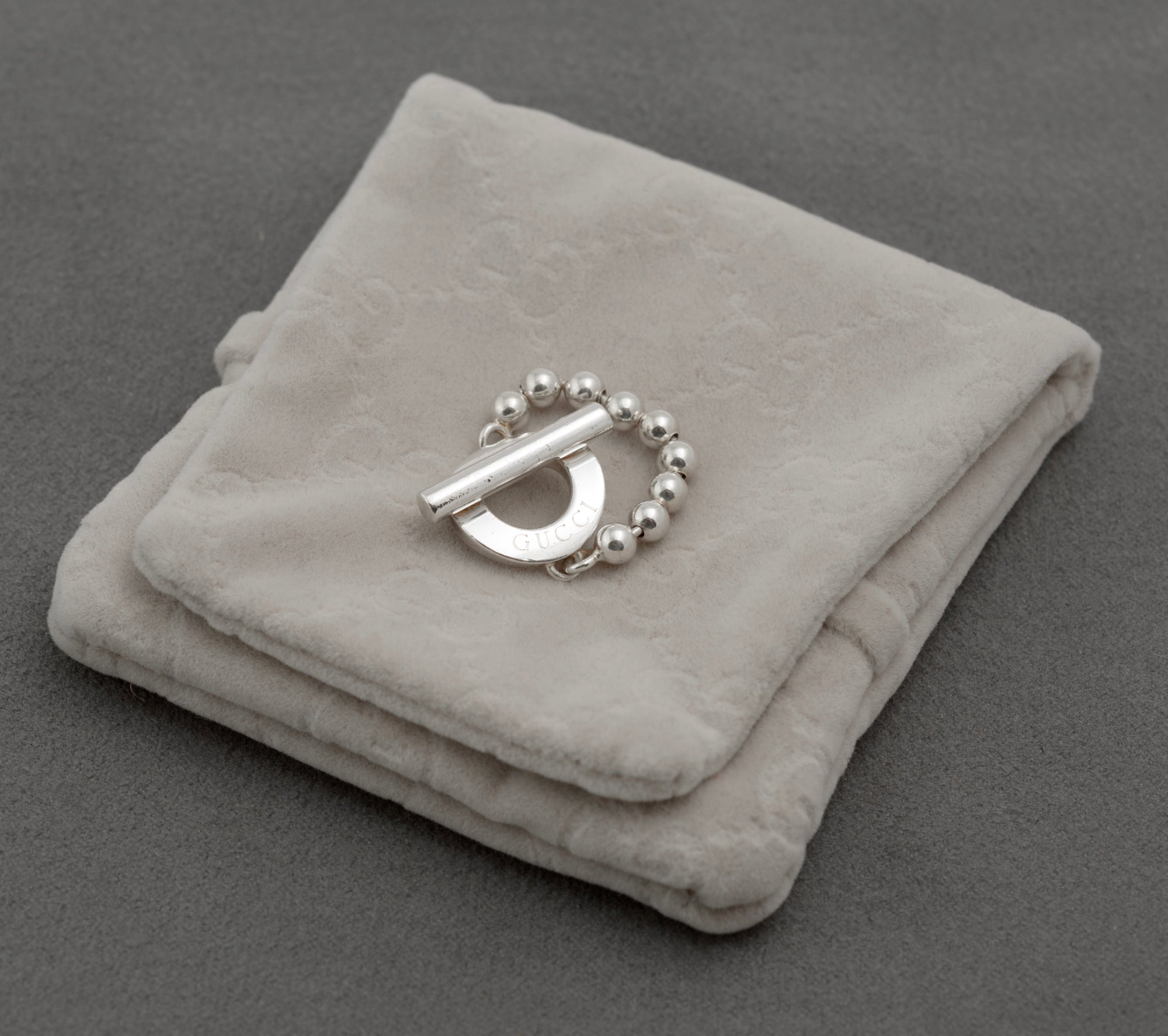 Gucci sterling silver Boule Toggle ring with flexible ball chain band resting on original Gucci grey suede pouch on dark grey background showing toggle front with GUCCI branding