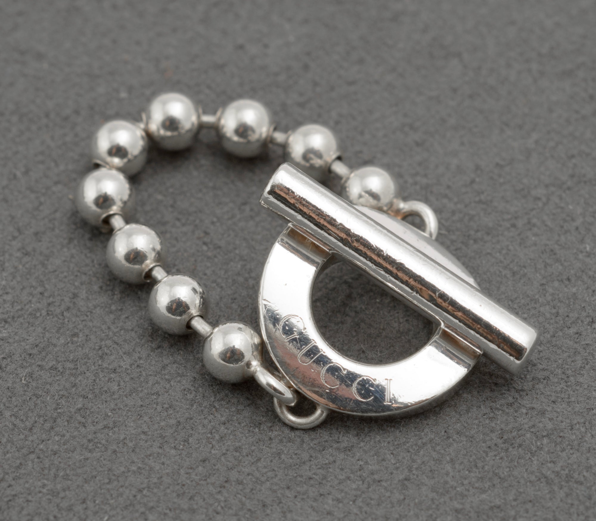 Gucci sterling silver Boule Toggle ring close up of front face showing circular toggle section with fixed polished silver T-bar and GUCCI branding in recessed lettering with ball chain band on dark grey background