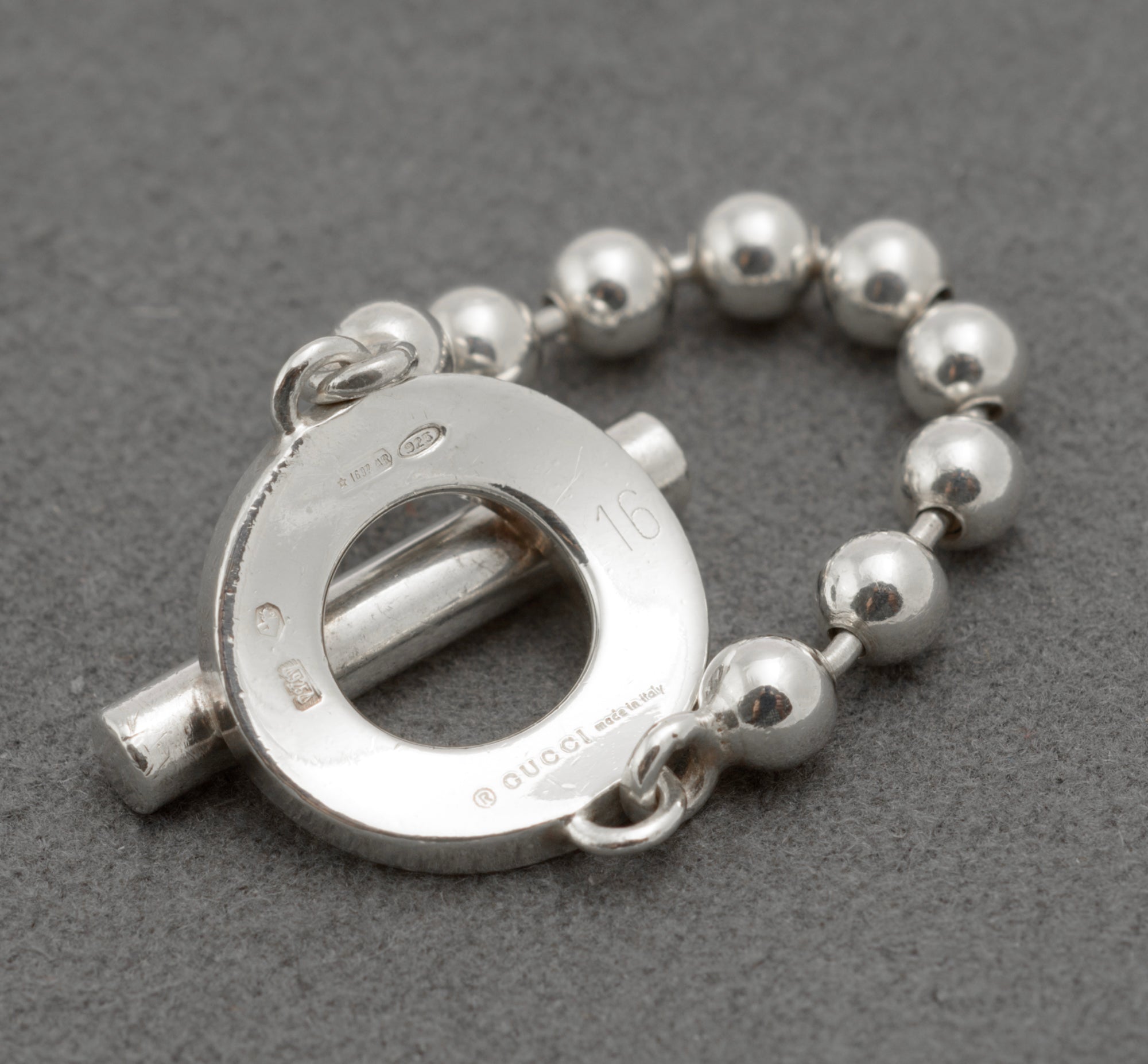 Reverse of Gucci sterling silver Boule Toggle ring showing copyright Gucci Made in Italy mark Italian hallmark 925 International Convention mark 1697 AR maker registration and EU size 16 stamp on dark grey background