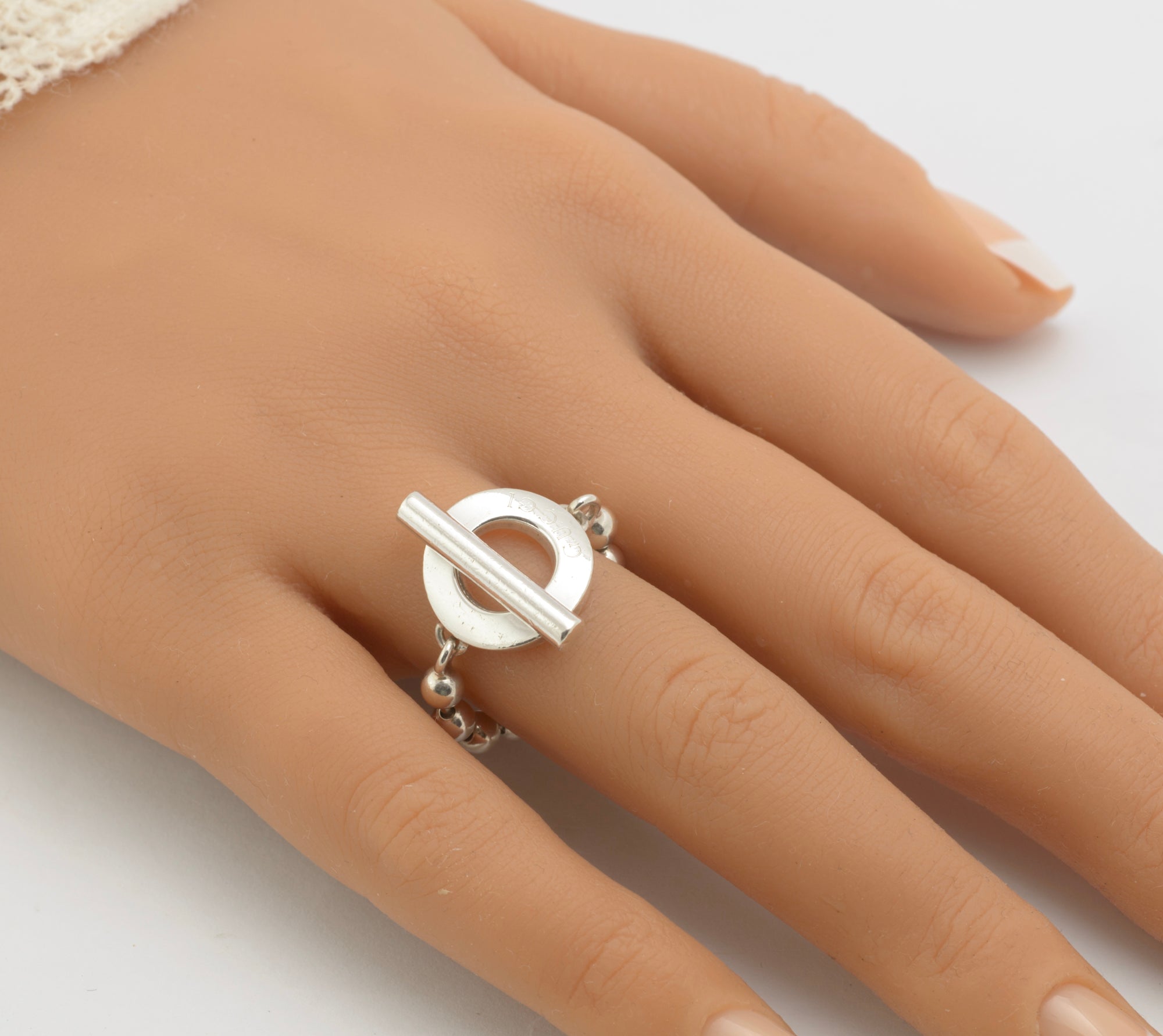Gucci sterling silver Boule Toggle ring worn on mannequin hand close up showing circular toggle front with T-bar and GUCCI branding with articulated ball chain band visible at sides on white background