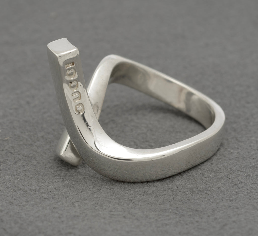 Gucci sterling silver crossover ring showing deeply punched GUCCI lettering on inner surface of upper diagonal bar with twisted band construction on grey background