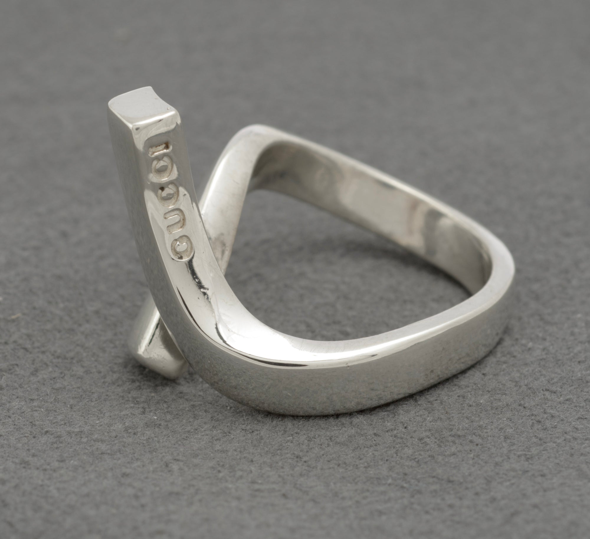 Gucci sterling silver crossover ring showing deeply punched GUCCI lettering on inner surface of upper diagonal bar with twisted band construction on grey background