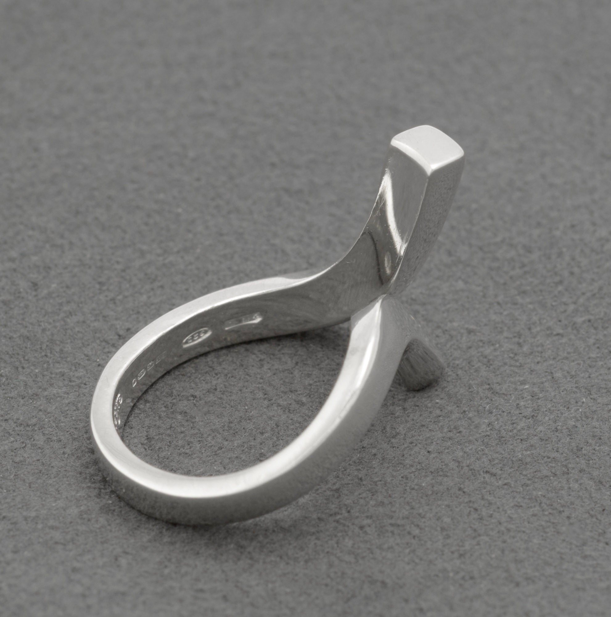 Inside band of Gucci sterling silver crossover ring showing hallmark suite including Gucci Made in Italy 925 Italian maker registration 419 AL and London sterling silver assay hallmark on grey background
