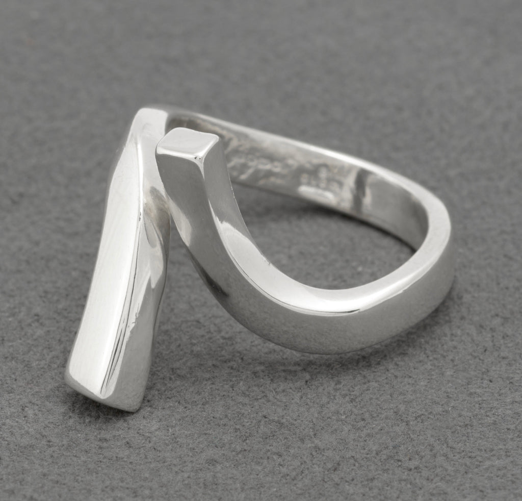 Three quarter front view of Gucci sterling silver crossover ring showing sculptural asymmetric twisted bar design with squared-off lower end and diagonal upper bar on grey background