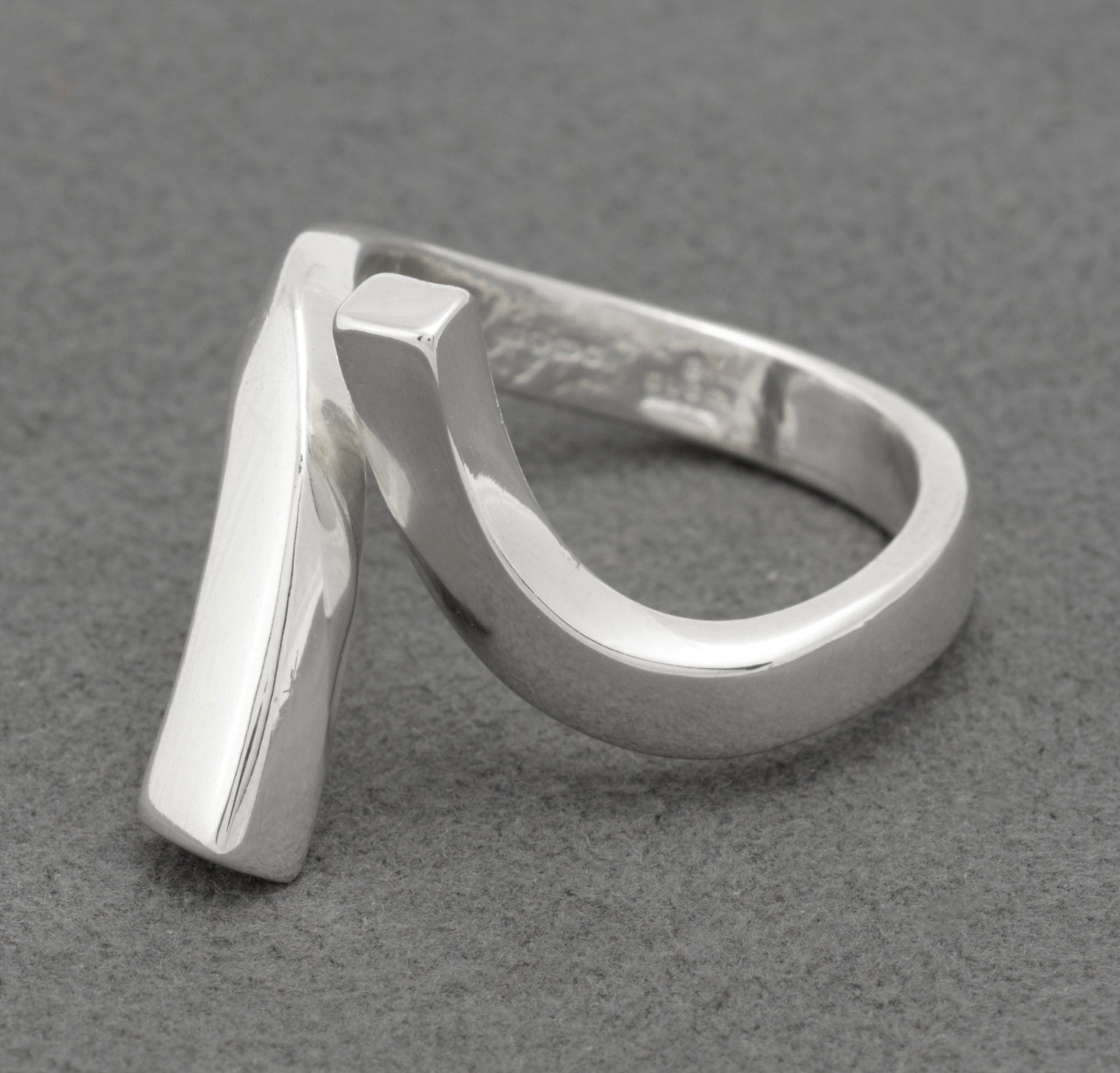 Three quarter front view of Gucci sterling silver crossover ring showing sculptural asymmetric twisted bar design with squared-off lower end and diagonal upper bar on grey background