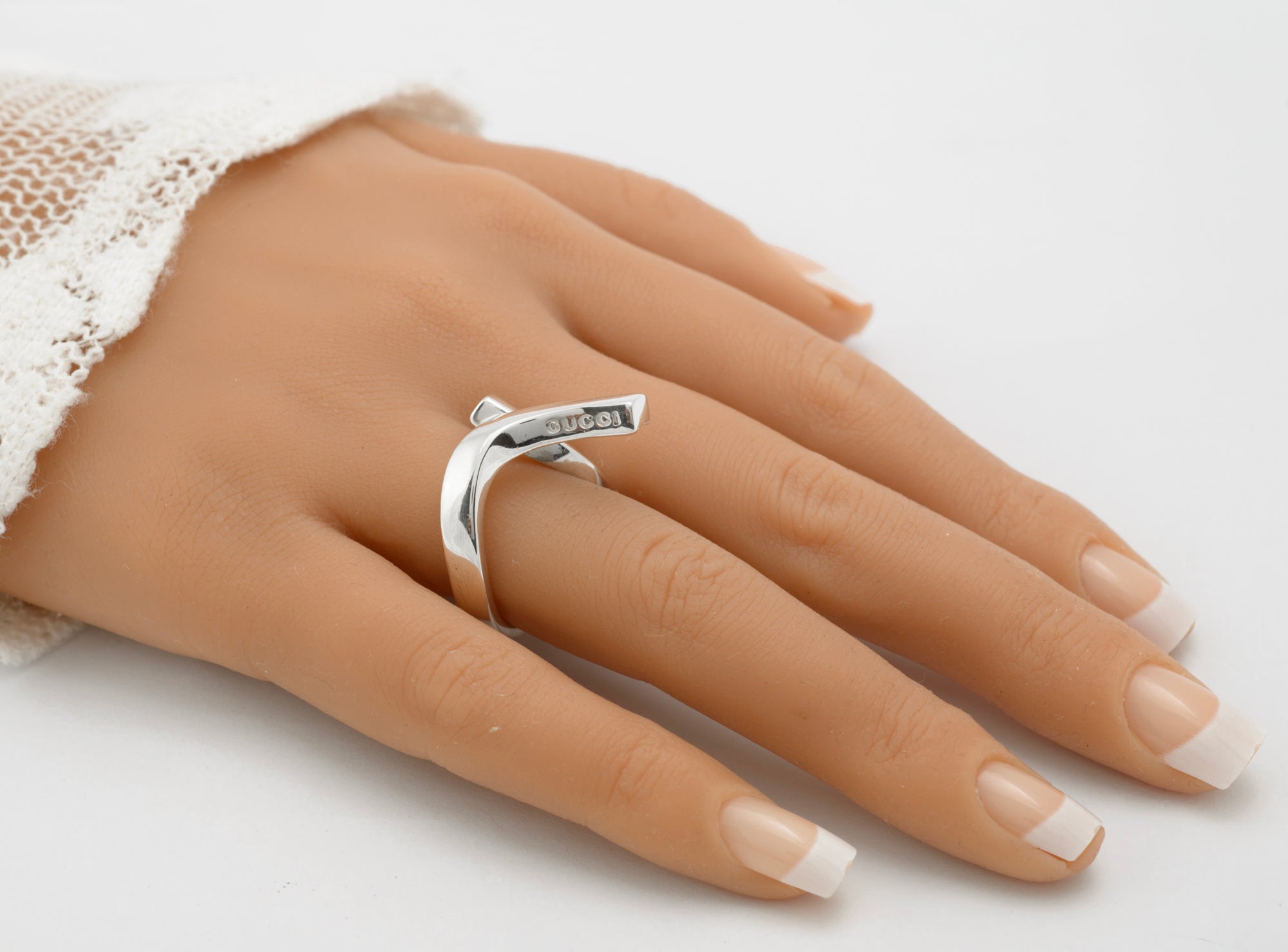 Gucci sterling silver crossover ring worn on mannequin finger showing diagonal branded bar riding across knuckle with GUCCI lettering visible on inner face on white background