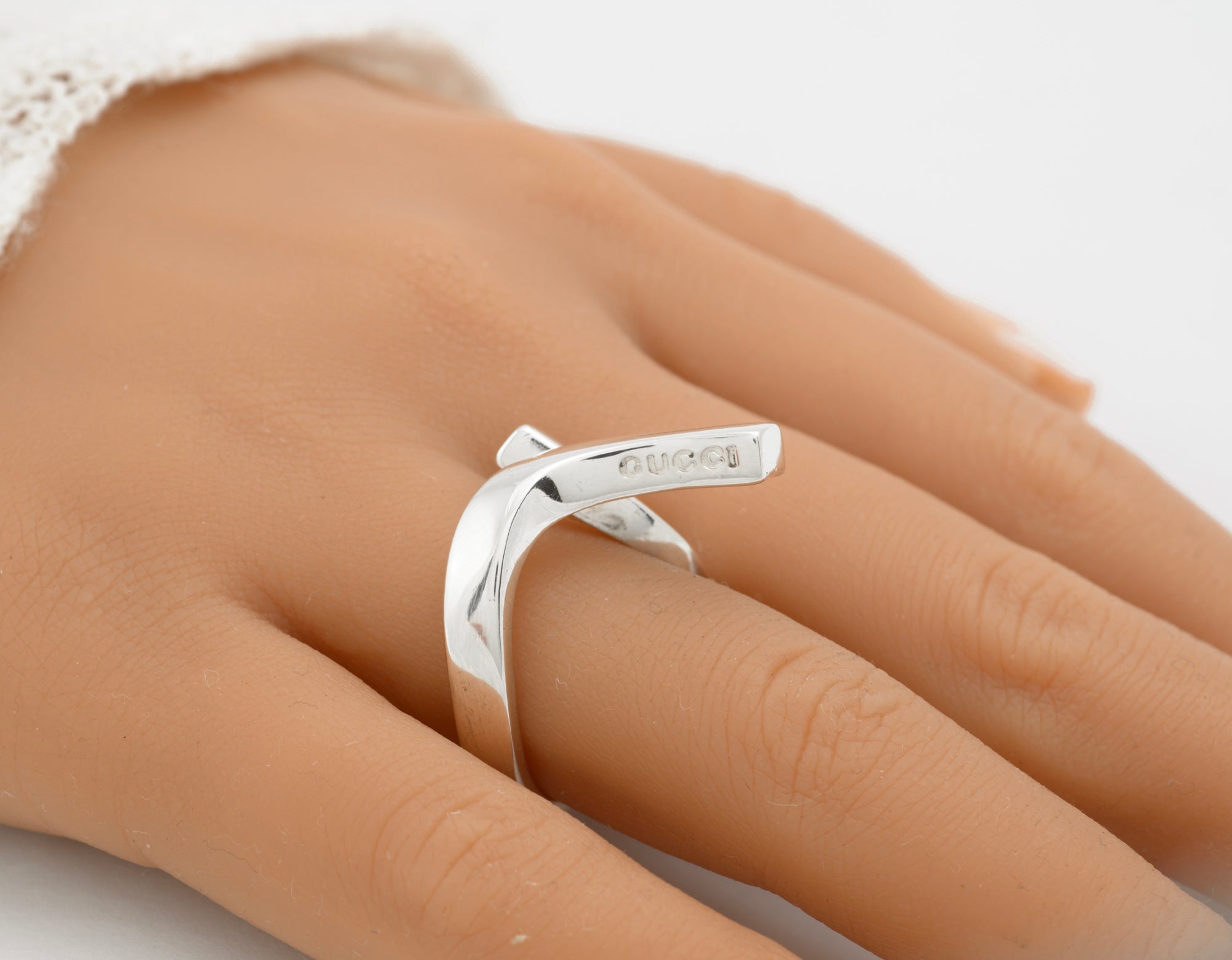 Gucci sterling silver crossover ring worn on mannequin finger side view showing sculptural twisted band construction with upper bar sitting diagonally across finger on white background