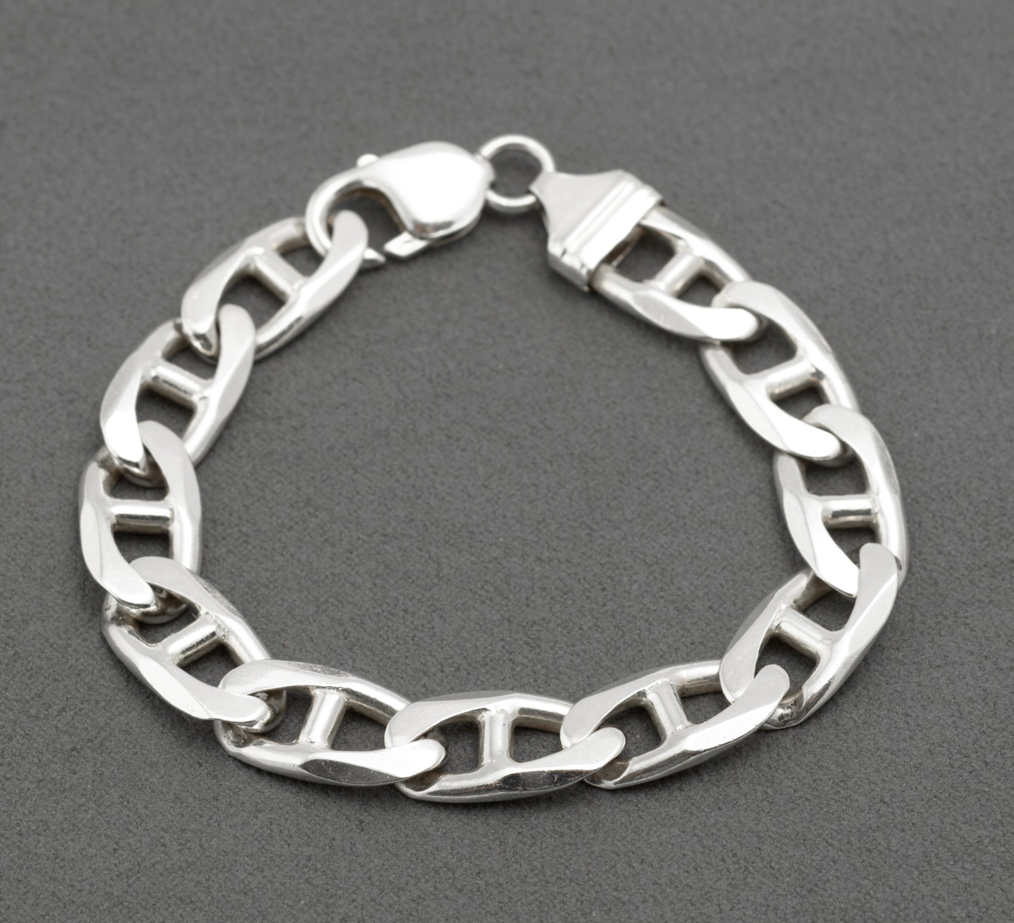 Vintage sterling silver broad mariner link bracelet laid in circle on dark grey background showing flat oval links with central dividing bars and lobster clasp with shaped ribbed terminal