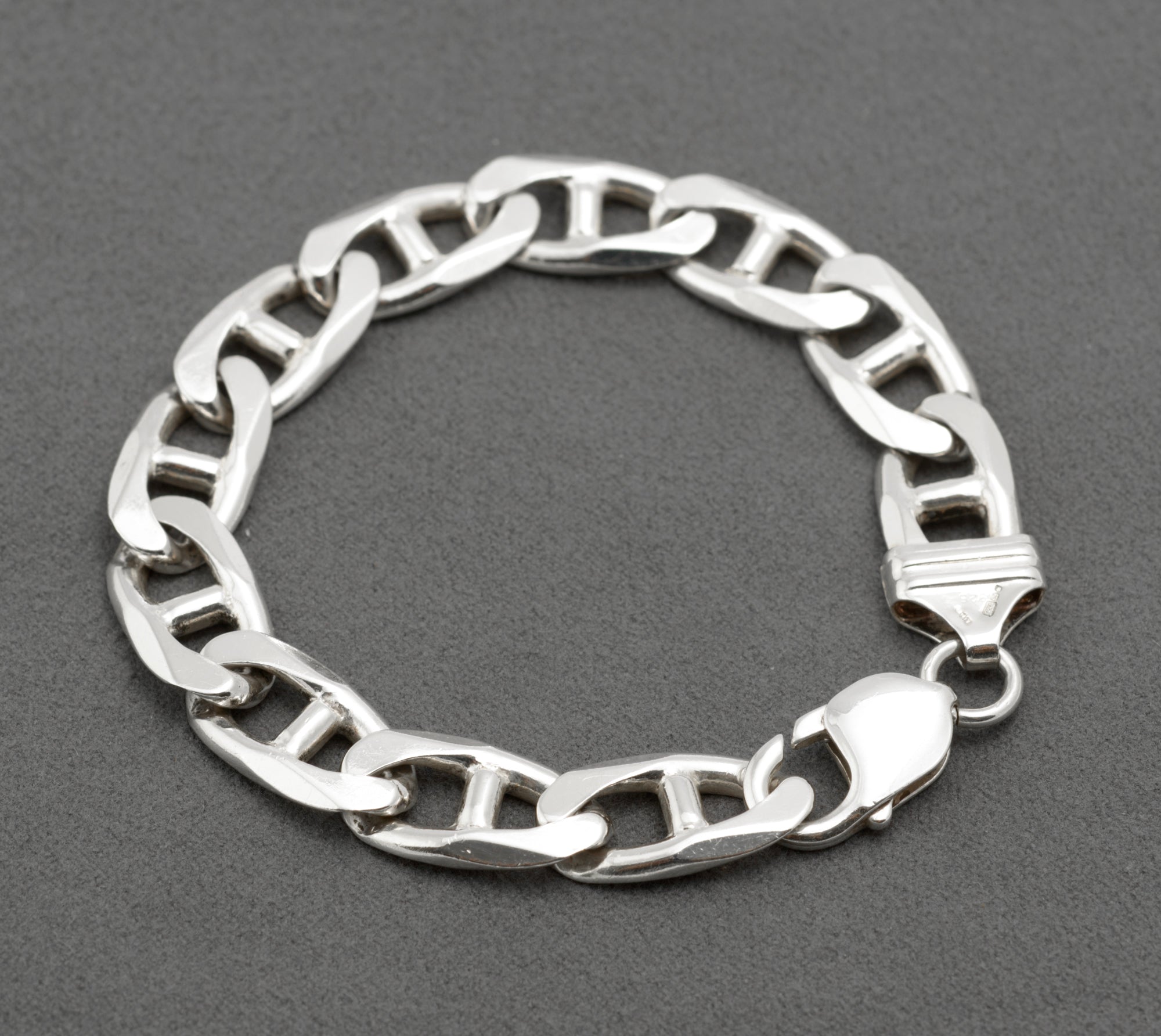 Vintage sterling silver mariner link bracelet laid in circle on dark grey background showing alternating link orientation and lobster clasp with connecting ring to shaped terminal