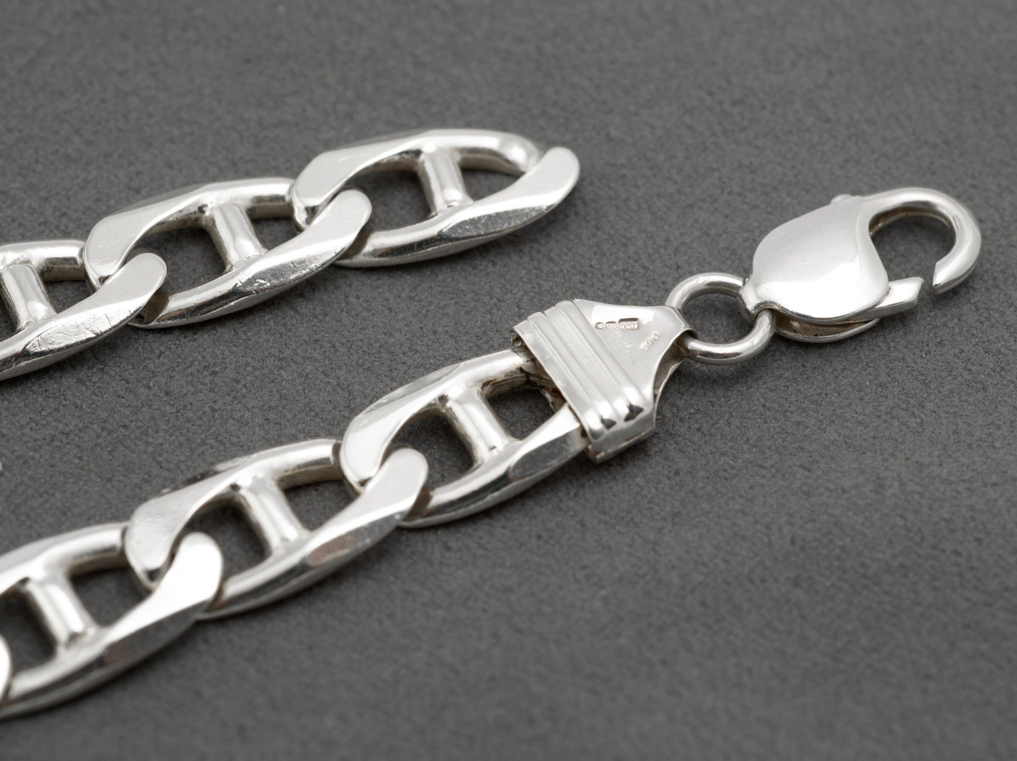 Close up of vintage sterling silver mariner link bracelet showing shaped ribbed end terminal with London International Convention hallmark and XPB sponsor mark and lobster clasp on dark grey background