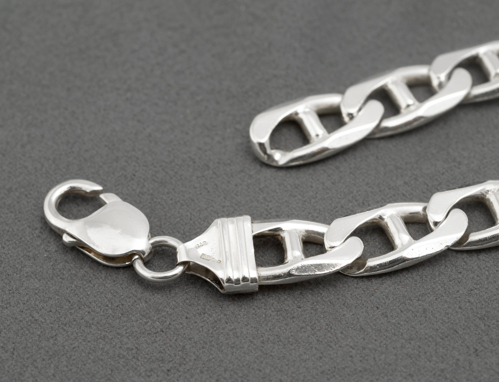 Close up of vintage sterling silver mariner link bracelet showing lobster clasp connecting ring and shaped ribbed terminal with hallmarks visible on dark grey background