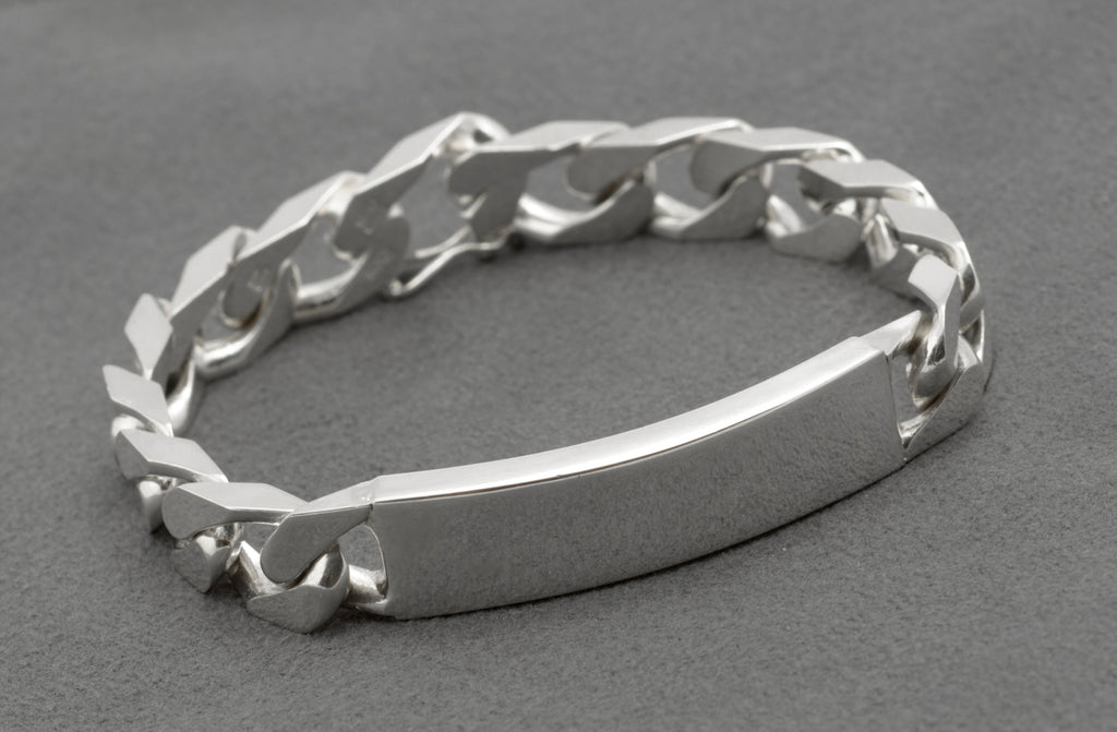 Italian sterling silver ID bracelet laid in circle on dark grey background showing reverse side of broad flattened curb links with push-piece box clasp and figure-8 safety catch visible