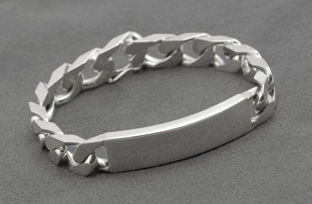 Italian sterling silver ID bracelet laid in circle on dark grey background showing reverse side of broad flattened curb links with push-piece box clasp and figure-8 safety catch visible