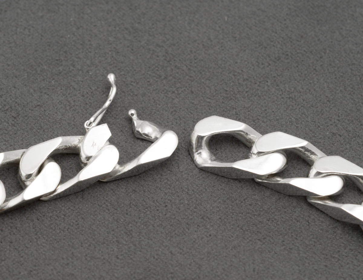 Close up of Italian sterling silver ID bracelet push-piece box clasp showing clasp link with Italy 925 and HPJ maker stamps and figure-8 safety catch in open position on dark grey background