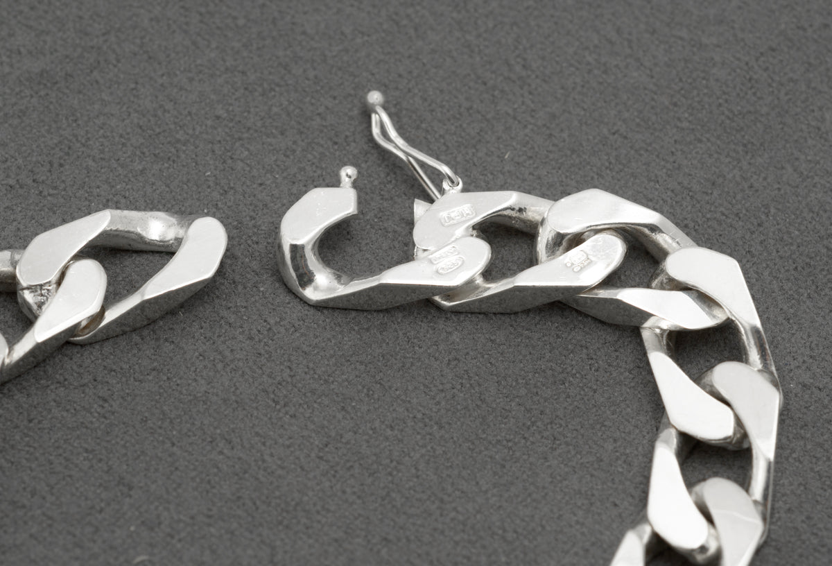 Italian sterling silver ID bracelet laid flat on dark grey background showing full 19.5cm length with plain unengraved curved ID panel push-piece clasp and broad flattened curb link chain