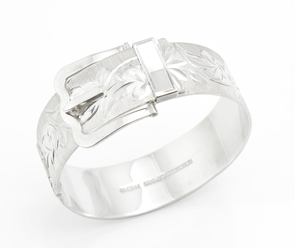A vintage sterling silver cuff bangle by Bracelon, hallmarked Birmingham 1976, fitted with an unusual patented buckle fastening. The broad textured band is decorated with bright cut scrolling foliate decoration, and the buckle face carries matching engraved detail. 49.6 grams.