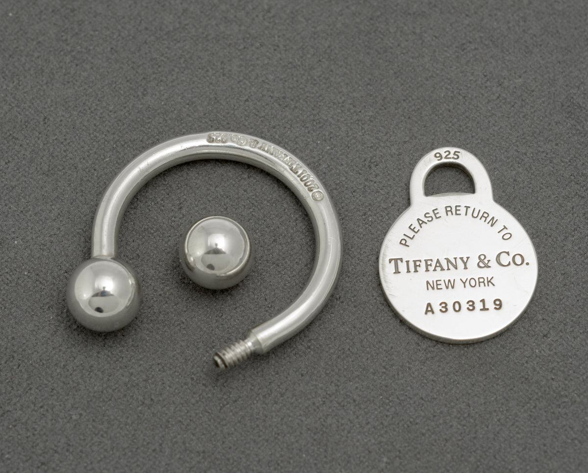 Tiffany and Co sterling silver screwball key ring disassembled showing ring with ball terminals and screw fitting alongside oval tag marked copyright Tiffany and Co 925