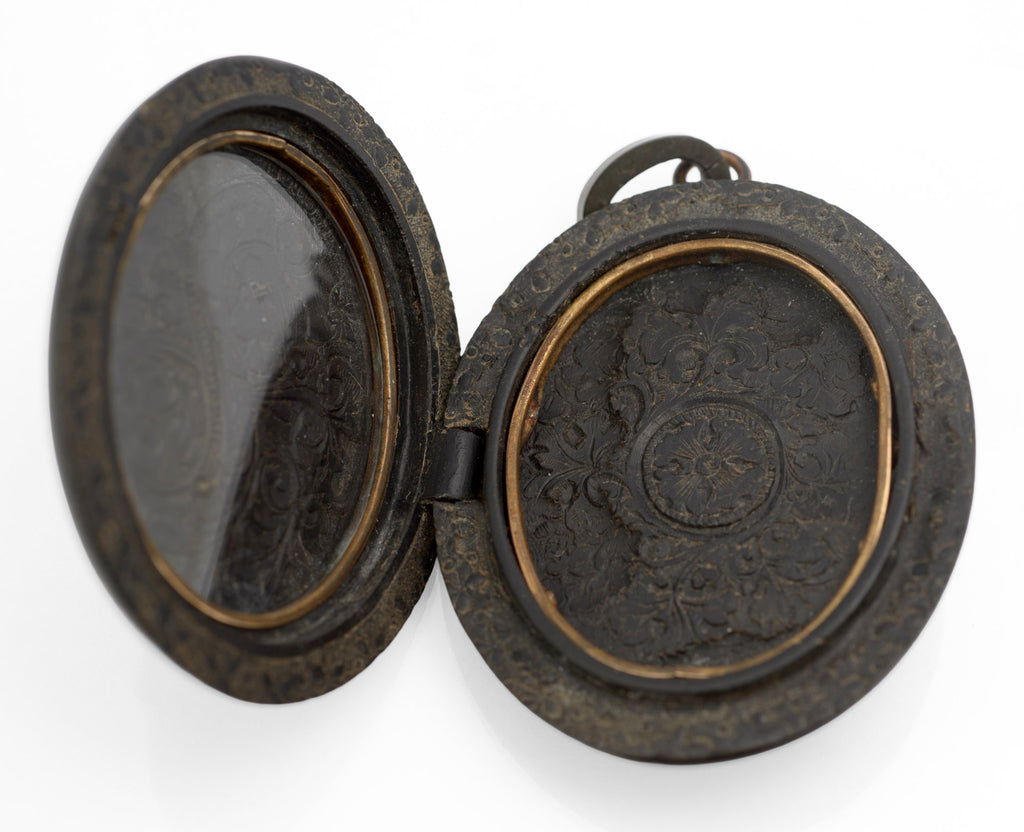 Antique Victorian vulcanite mourning locket full front view on white background showing overall oval form and cross decoration with foliate scrolls