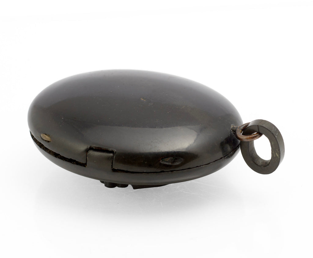 Antique Victorian vulcanite mourning locket open view showing both halves with finely patterned interior, brass retaining rings and original domed glazed cover