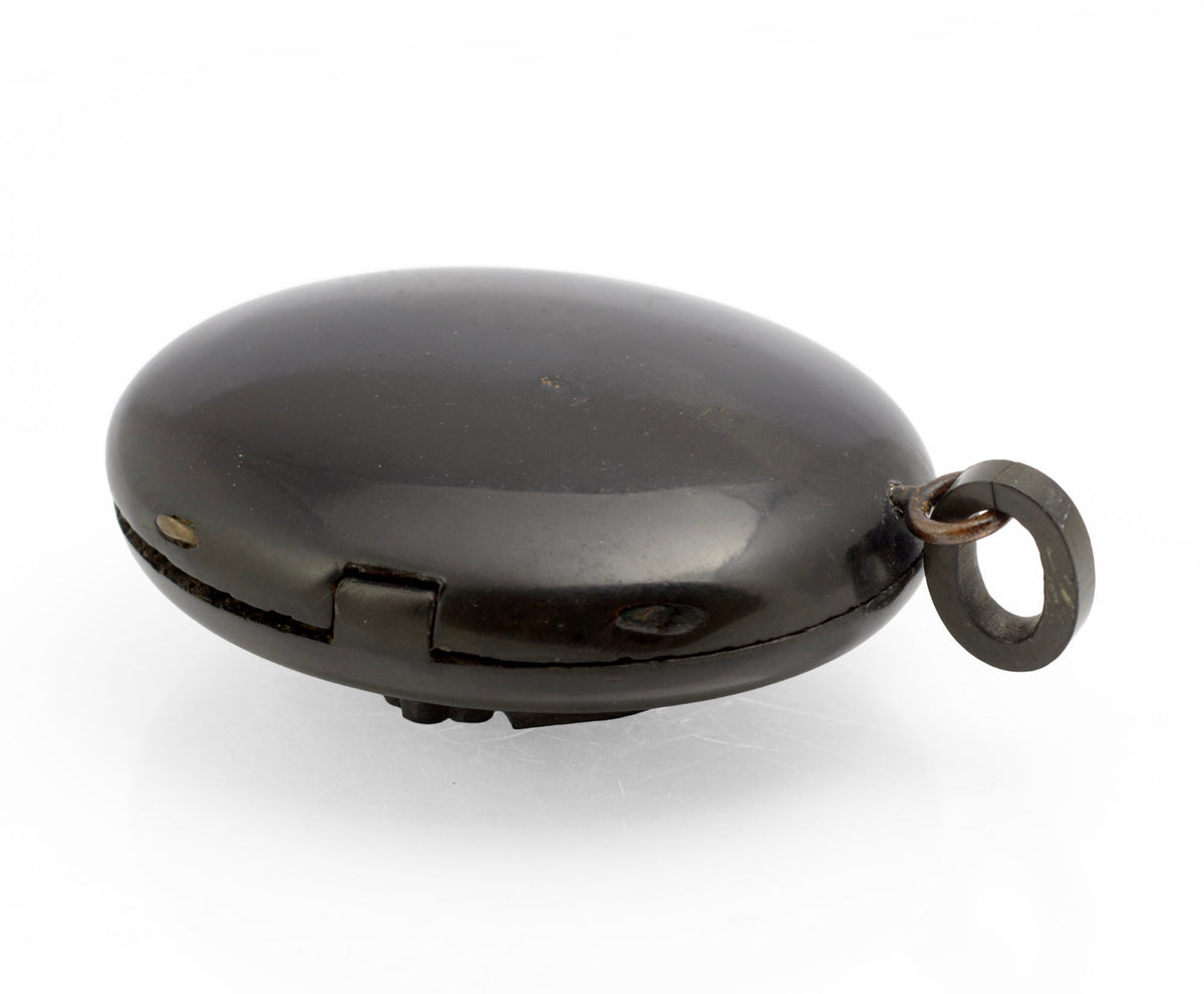 Antique Victorian vulcanite mourning locket open view showing both halves with finely patterned interior, brass retaining rings and original domed glazed cover
