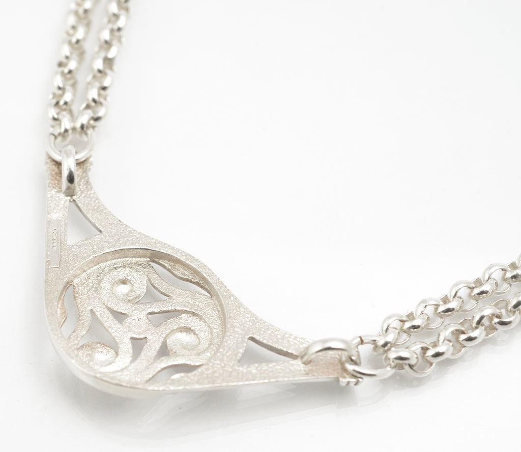 Vintage Ola Gorie sterling silver necklet side view on grey background showing depth of openwork triskelion centre and wire wrapped chain attachment