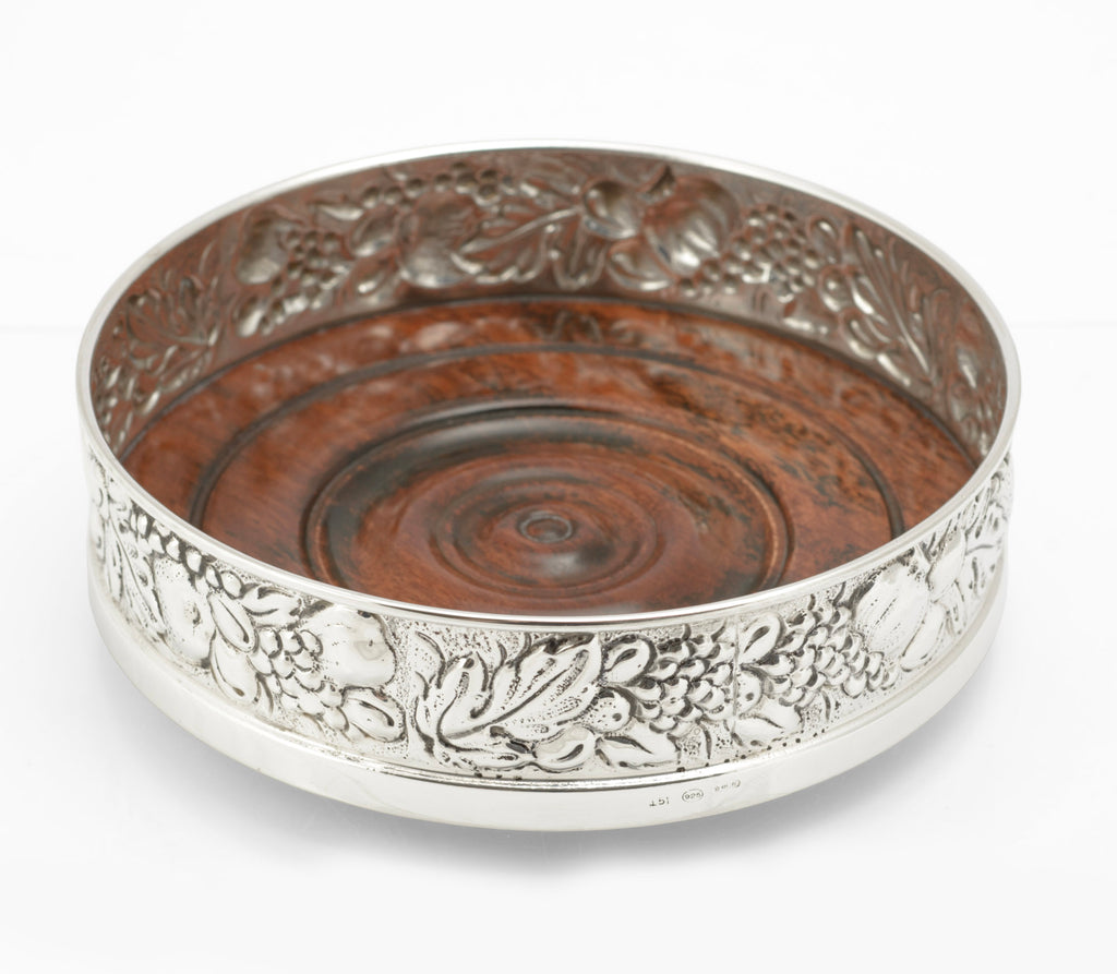 Sterling silver repousse bottle coaster by Falsini Ferruccio Florence, grapevine decoration, turned hardwood base - three quarter view