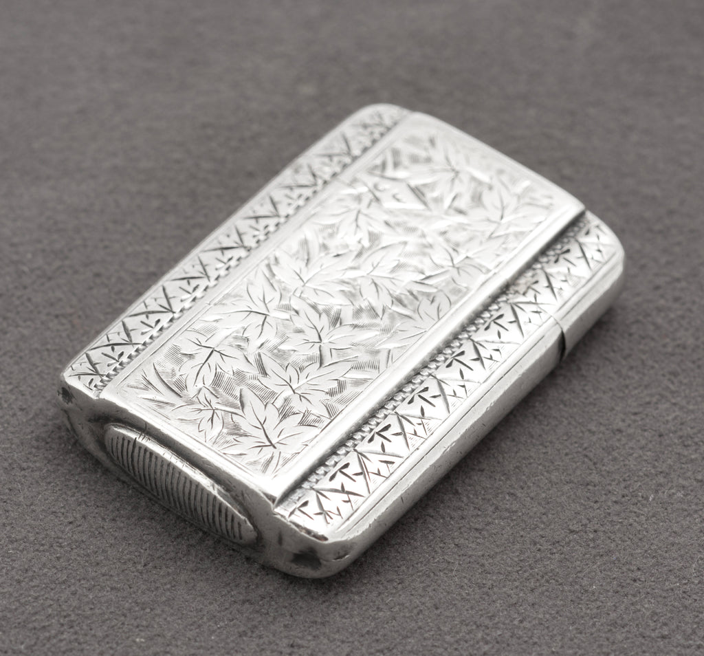 Close view of the leaves, scrollwork and geometric border decoration on the sterling silver vesta case