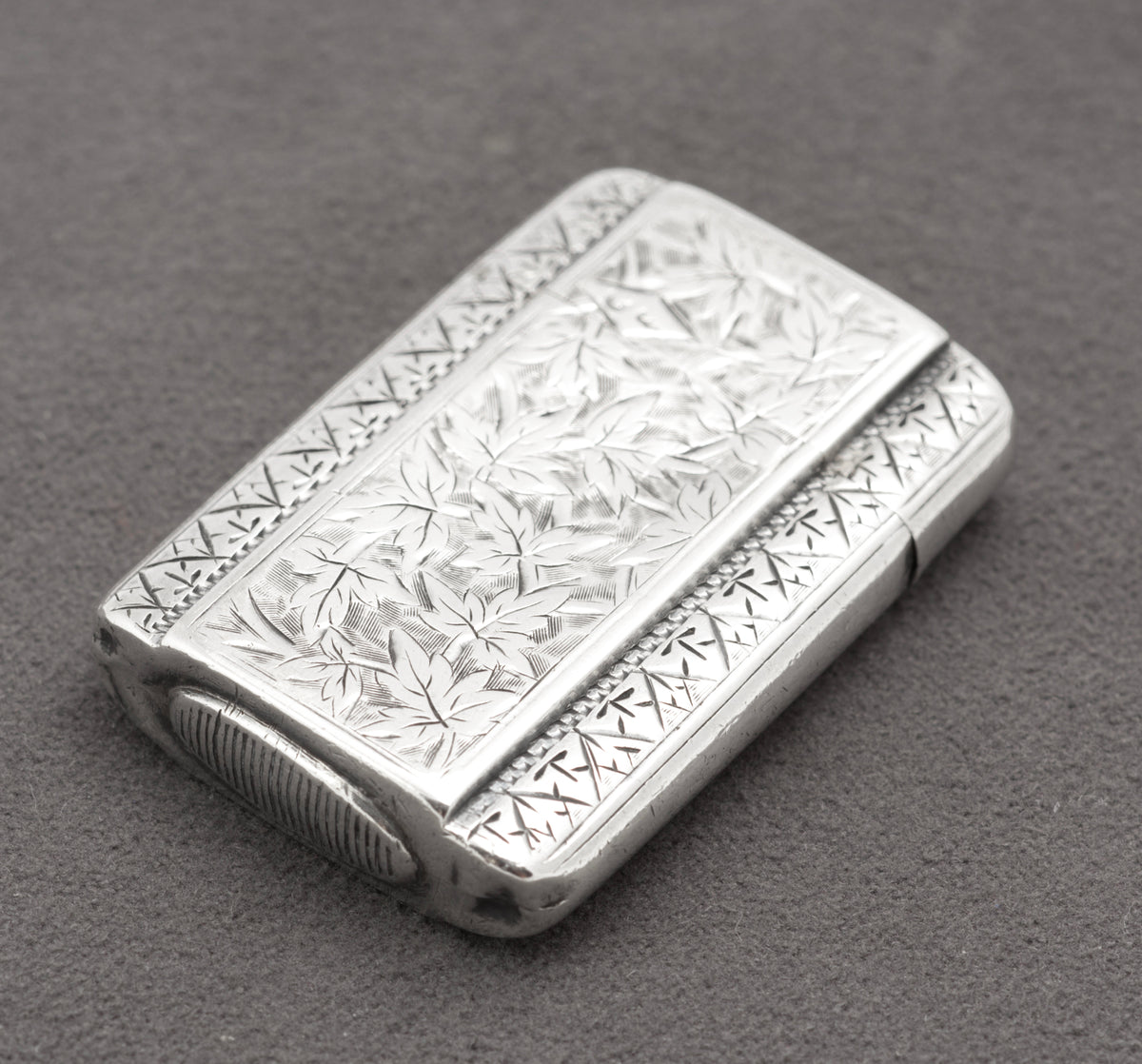 Close view of the leaves, scrollwork and geometric border decoration on the sterling silver vesta case