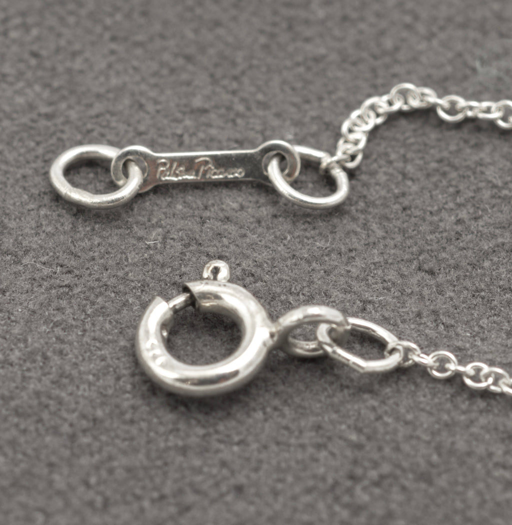 Full length of Tiffany Paloma Picasso Kiss necklace laid out on grey - C3111