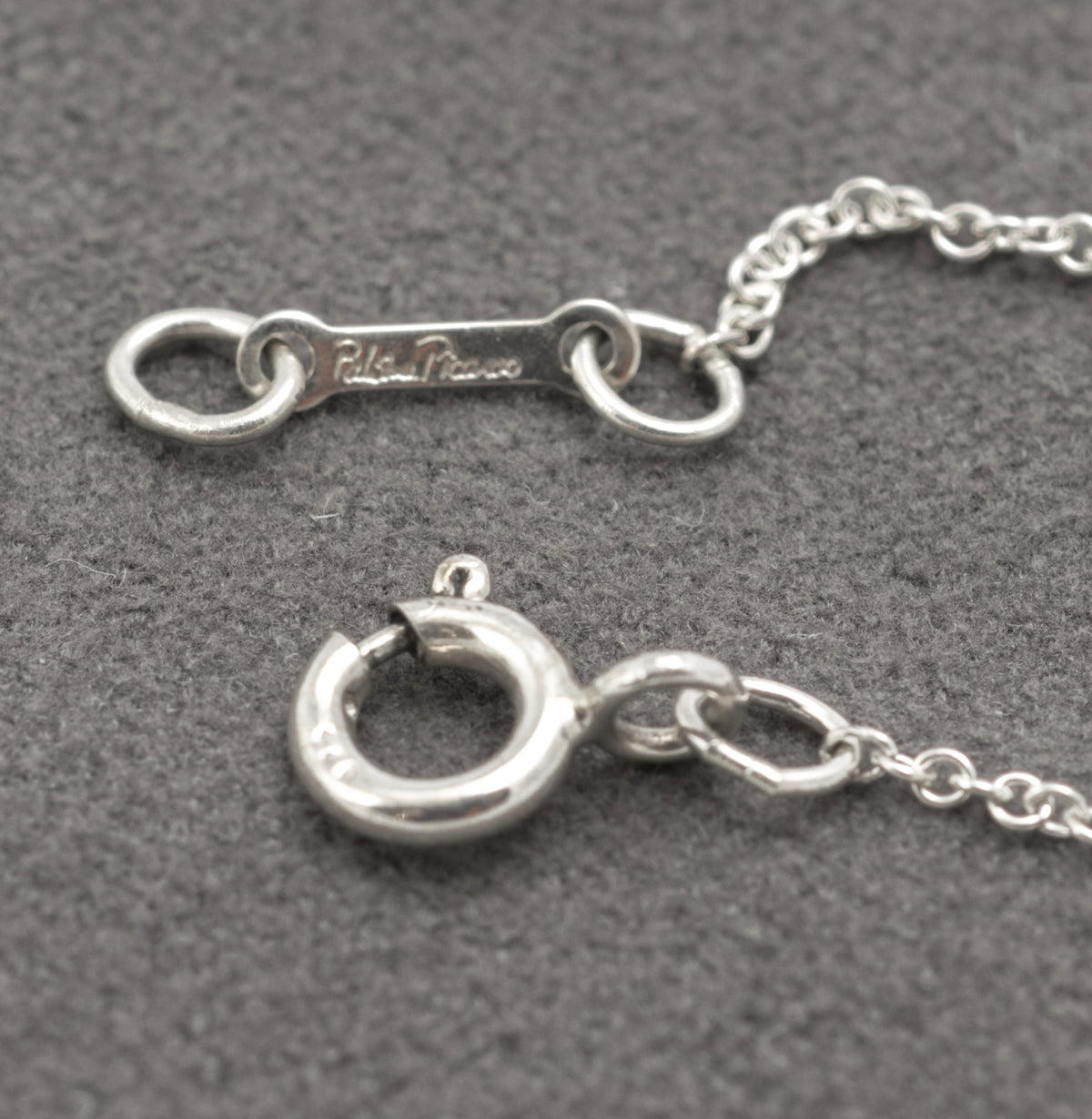 Full length of Tiffany Paloma Picasso Kiss necklace laid out on grey - C3111