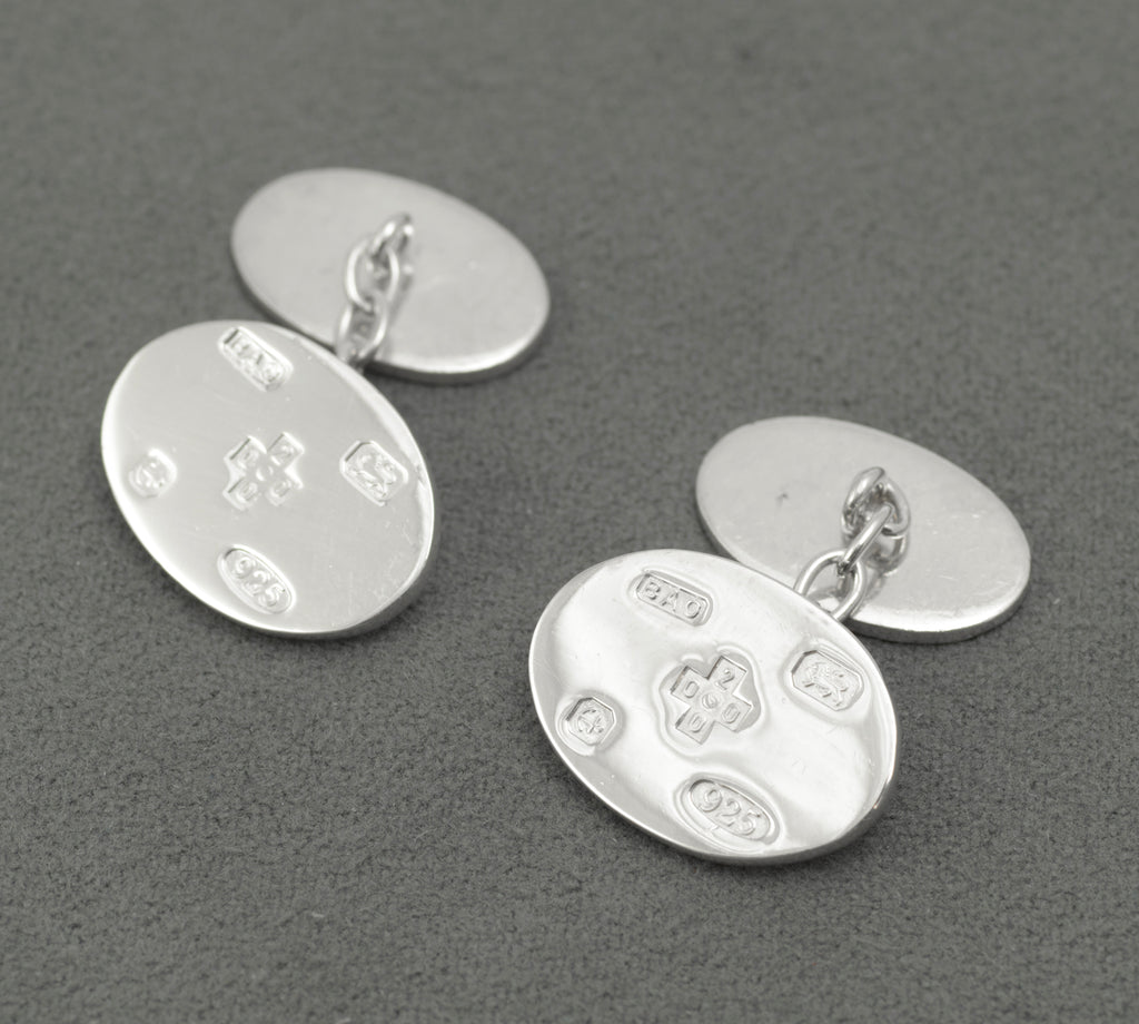 A pair of sterling silver oval cufflinks displaying the special Birmingham millennium hallmark arrangement for the year 2000. The fronts carry feature marks, including the millennium cross, together with the Birmingham Assay Office sponsor mark.