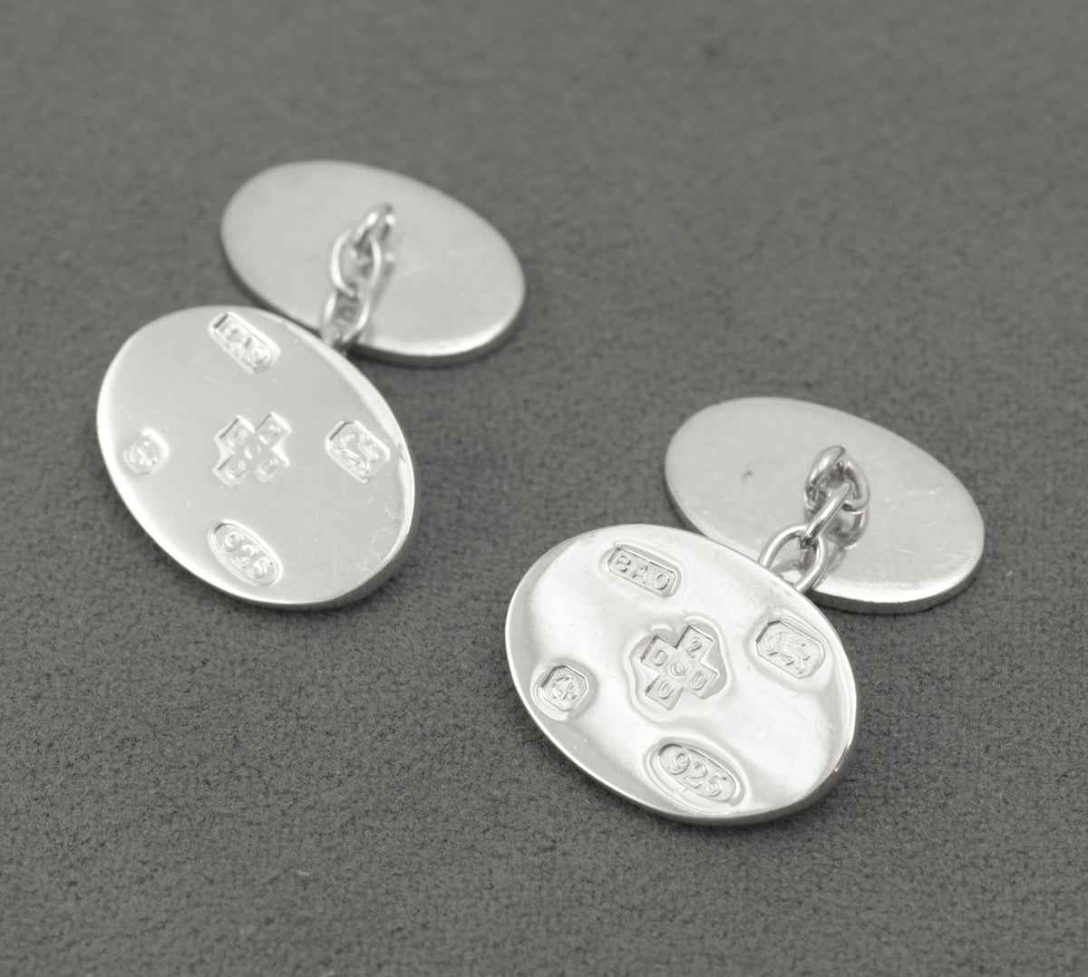 A pair of sterling silver oval cufflinks displaying the special Birmingham millennium hallmark arrangement for the year 2000. The fronts carry feature marks, including the millennium cross, together with the Birmingham Assay Office sponsor mark.