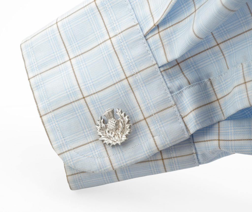 Silver thistle cufflink displayed through a blue checked shirt cuff
