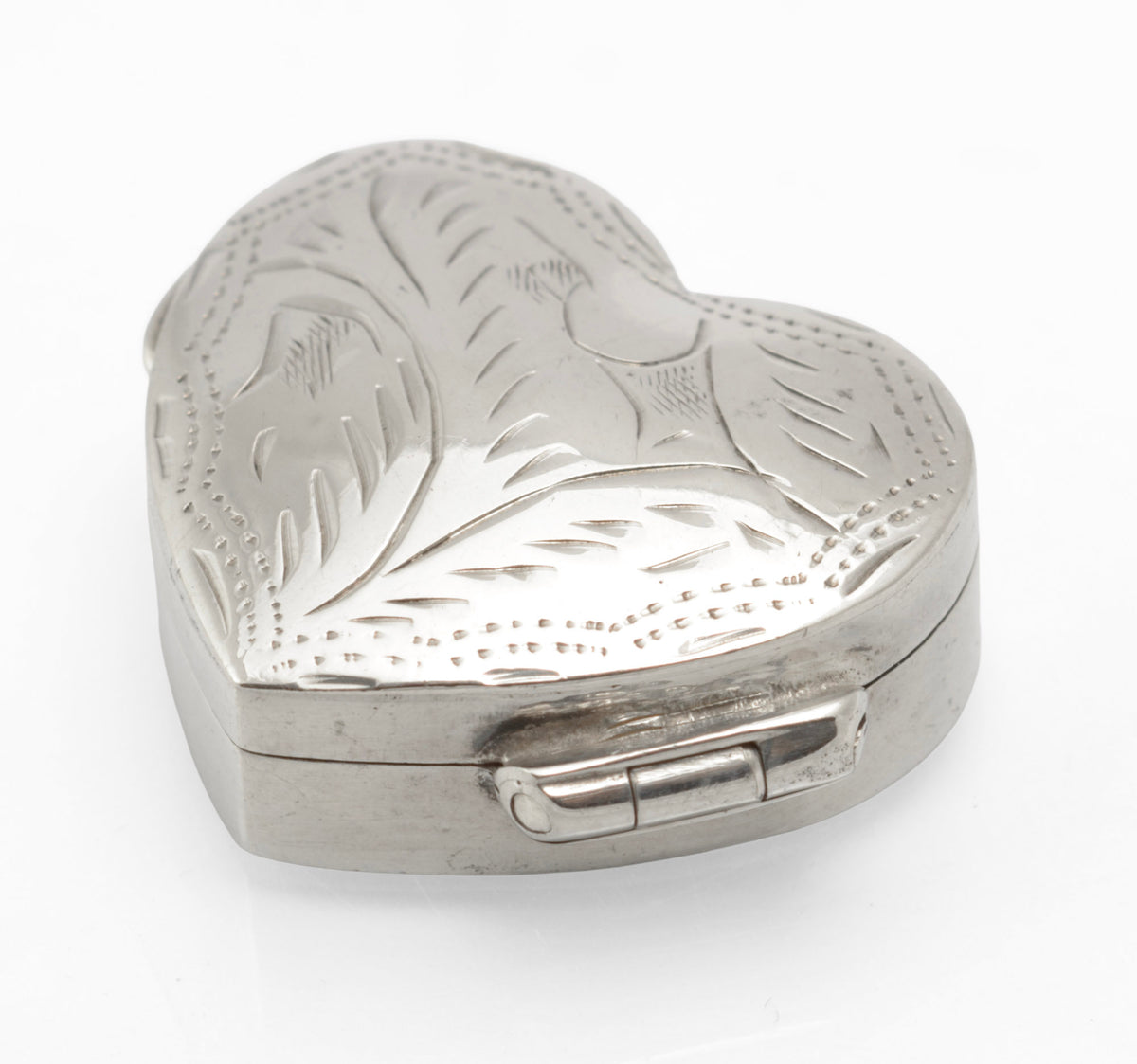 Angled view of the engraved heart shaped silver pill box showing its hinge and plain sides